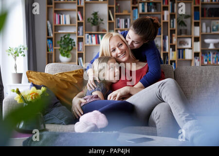 Mutter und ihre Töchter kuscheln und Spaß haben, sitzen auf der Couch Stockfoto