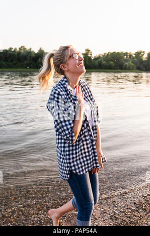 Lachende junge Frau zu Fuß auf Riverside am Abend Stockfoto