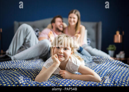 Freche kleines Mädchen auf dem Bett liegend mit ihren Eltern Stockfoto