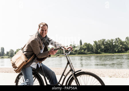 Reifer Mann mit Fahrrad mit an Rhein Ufer smartphone Stockfoto
