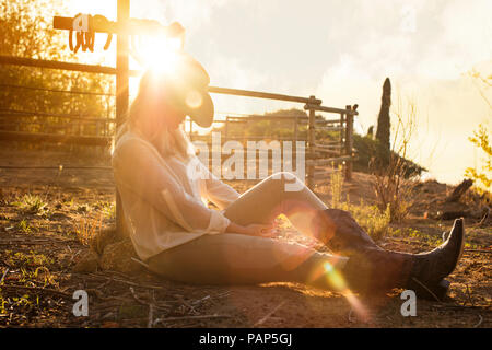 Frau sitzt auf einem Bauernhof bei Sonnenuntergang Stockfoto