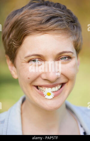 Portrait von lachende Frau mit Daisy im Mund