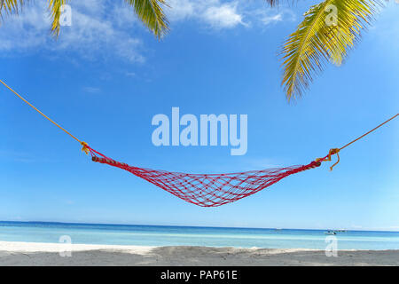 Rote Seil Hängematte zwischen Palmen an einem unberührten, weißen Sandstrand, mit türkisblauem Meer - Bohol, Philippinen. Stockfoto