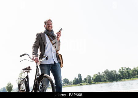 Reifer Mann mit Fahrrad mit an Rhein Ufer smartphone Stockfoto