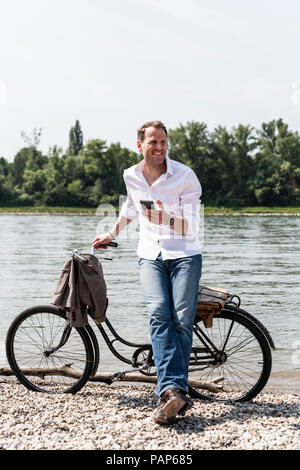 Reifer Mann mit Fahrrad mit an Rhein Ufer smartphone Stockfoto