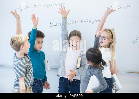 Glückliche Schüler heben ihre Hände an der Tafel mit Formeln in der Klasse Stockfoto