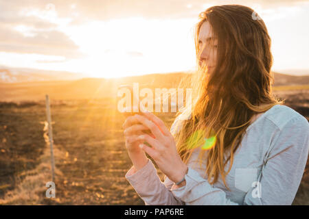 Island, Frau, die bei Sonnenuntergang smartphone Stockfoto