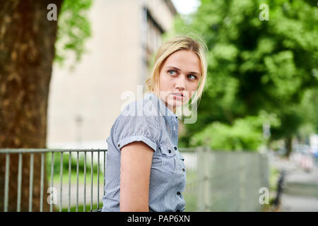 Ernsthafte blonde junge Frau an einem Zaun Stockfoto