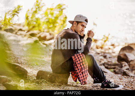 Junger Mann, der Baseball Cap in der Natur sitzen Stockfoto