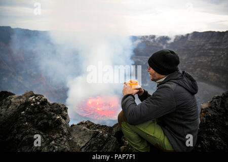 Afrika, Demokratische Republik Kongo, Virunga National Park, Mann sittiing über Vulkan Nyiragongo Krater Stockfoto