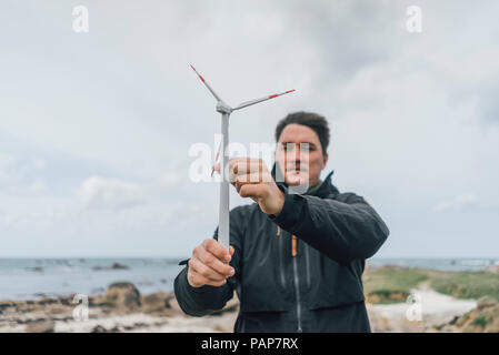 Frankreich, Bretagne, Meneham, Mann mit Miniatur Wind Turbine an der Küste Stockfoto