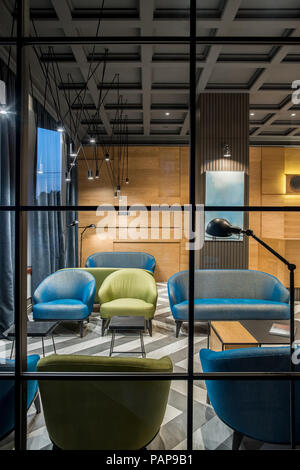Beleuchteter Innenraum im Hotel mit dunklen Decke und gemusterten Fliesenboden. Es ist eine hölzerne Rezeption, Spalte, bunten Sesseln und Sofas, Stockfoto