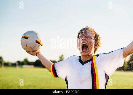 Junge tragen Deutsche Fussball shirt schreien vor Freude, stehend im Wasser spritzt Stockfoto