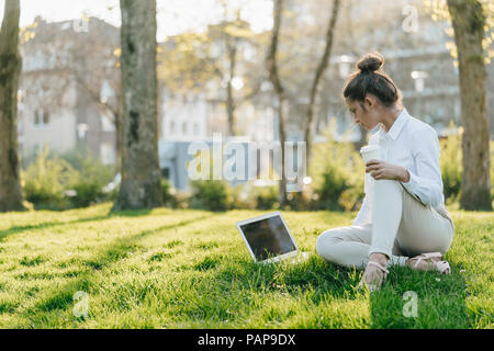 Junge Geschäftsfrau, die brechen, mit Laptop, sitzen im Gras und trinken Kaffee Stockfoto