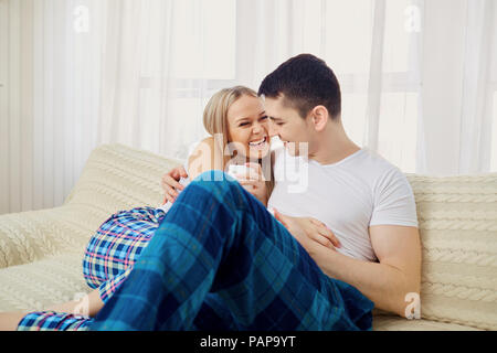 Ein Kerl und ein Mädchen im Schlafanzug sind umarmen Sitzen auf der Couch in Stockfoto