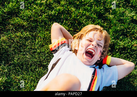 Junge im deutschen Fussball shirt liegen auf Gras, laughimg Stockfoto