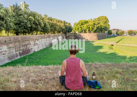 Person mit einer Flasche Bier auf die historischen Stadtmauern von Lucca, Toskana, Italien, mit Bewunderung auf die umliegende Landschaft. Stockfoto