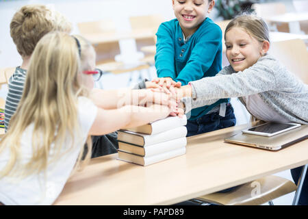 Glückliche Schüler stapeln Hände auf Bücher in der Klasse Stockfoto