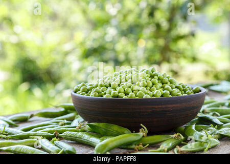 Geschälte grüne Erbsen in einer Platte auf einem Holztisch. Es liegt neben der pea Pods. Horisontal Foto Stockfoto