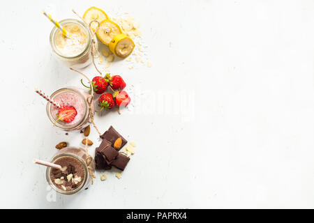 Satz von milchshake in Töpfen. Banane Schoko und Erdbeere Milchshakes mit Muttern und Kokosnuss. Sommer Nachtisch. Gesundes Essen. Ansicht von oben. Stockfoto