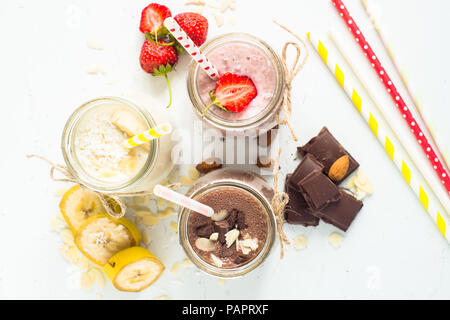 Satz von milchshake in Töpfen. Banane Schoko und Erdbeere Milchshakes mit Muttern und Kokosnuss. Sommer Nachtisch. Ansicht von oben. Stockfoto