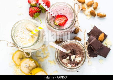 Satz von milchshake in Töpfen. Banane Schoko und Erdbeere Milchshakes mit Muttern und Kokosnuss. Sommer Nachtisch. Ansicht von oben. Stockfoto