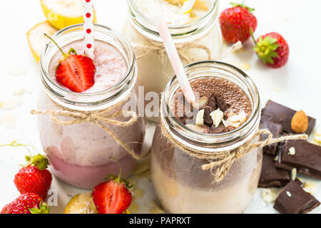 Satz von milchshake in Töpfen. Banane Schoko und Erdbeere Milchshakes mit Muttern und Kokosnuss. Sommer Nachtisch. Gesundes Essen. Stockfoto