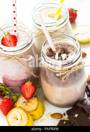 Satz von milchshake in Töpfen. Banane Schoko und Erdbeere Milchshakes mit Muttern und Kokosnuss. Sommer Nachtisch. Gesundes Essen. Vertikale. Stockfoto