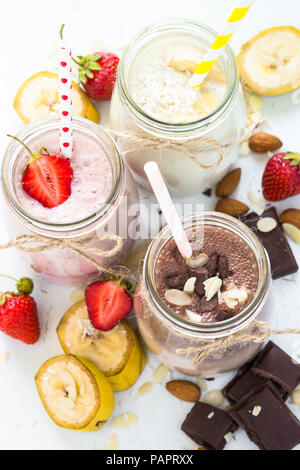 Satz von milchshake in Töpfen. Banane Schoko und Erdbeere Milchshakes mit Muttern und Kokosnuss. Sommer Nachtisch. Gesundes Essen. Vertikale. Stockfoto