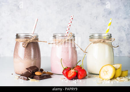 Satz von milchshake in Töpfen. Banane Schoko und Erdbeere Milchshakes mit Muttern und Kokosnuss. Sommer Nachtisch. Gesundes Essen. Stockfoto