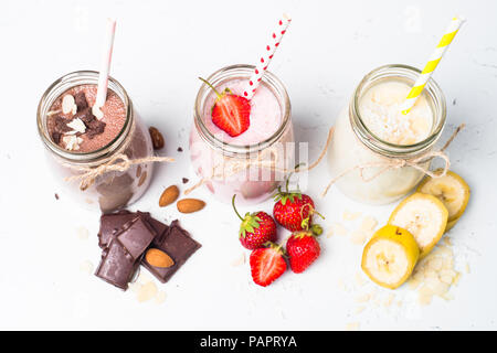 Satz von milchshake in Töpfen. Banane Schoko und Erdbeere Milchshakes mit Muttern und Kokosnuss auf Weiß. Sommer Nachtisch. Gesundes Essen. Ansicht von oben. Stockfoto