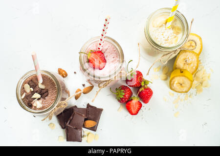 Satz von milchshake in Töpfen. Banane Schoko und Erdbeere Milchshakes mit Muttern und Kokosnuss. Sommer Nachtisch. Gesundes Essen. Ansicht von oben. Stockfoto
