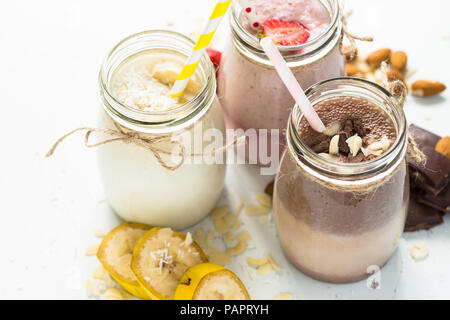 Satz von milchshake in Töpfen. Banane Schoko und Erdbeere Milchshakes mit Muttern und Kokosnuss. Sommer Nachtisch. Gesundes Essen. Stockfoto