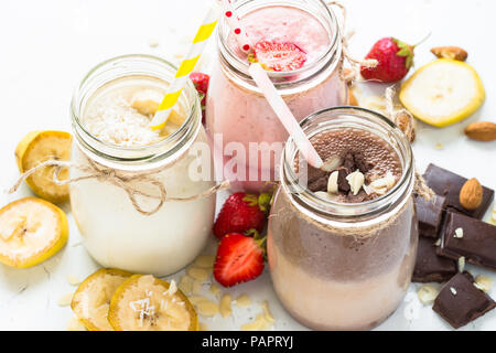Satz von milchshake in Töpfen. Banane Schoko und Erdbeere Milchshakes mit Muttern und Kokosnuss. Sommer Nachtisch. Gesunde Ernährung auf Weiß. Stockfoto