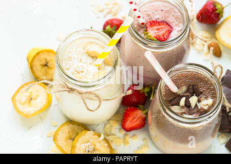 Satz von milchshake in Töpfen. Banane Schoko und Erdbeere Milchshakes mit Muttern und Kokosnuss. Sommer Nachtisch. Gesundes Essen. Stockfoto
