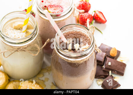 Satz von milchshake in Töpfen. Banane Schoko und Erdbeere Milchshakes mit Muttern und Kokosnuss. Sommer Nachtisch. Gesundes Essen. Close Up. Stockfoto