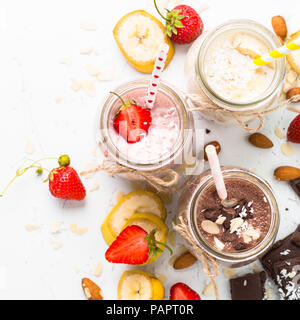 Satz von milchshake in Töpfen. Banane, Schokolade und Erdbeeren Milchshakes mit Muttern und Kokosnuss. Gesundes Essen. Draufsicht auf Weiß. Stockfoto