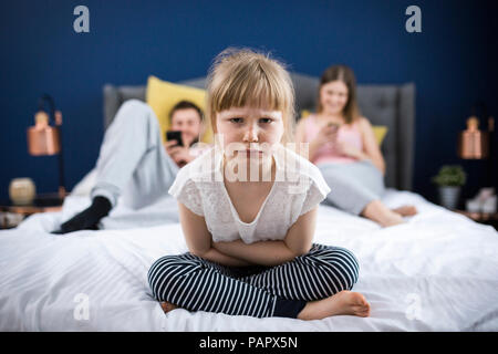 Böse Mädchen sitzen auf dem Bett mit ihren Eltern Stockfoto