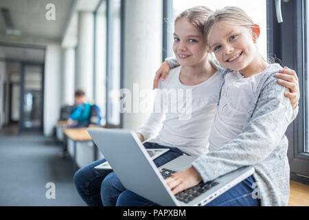 Portrait von zwei lächelnde Schülerinnen mit Notebook und Tablet-PC umarmt Stockfoto