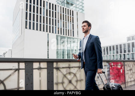 Junge Unternehmer mit Handy und rollenden Koffer in der Stadt unterwegs. Stockfoto