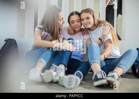 Lächelnde Mädchen sitzt auf dem Boden in der Schule umarmen Stockfoto