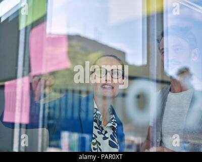 Kollegen suchen bei kurznotiz an der Glasscheibe Stockfoto