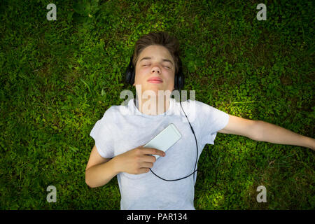 Portrait von Jungen liegen auf Wiese Musik hören mit Kopfhörern und Smartphone Stockfoto