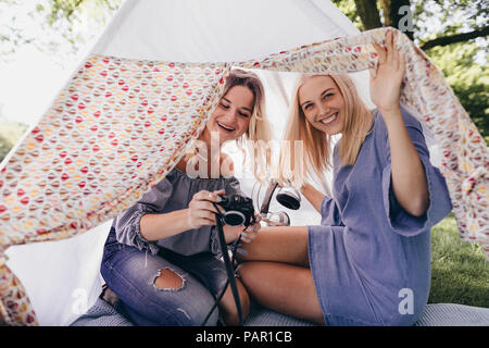 Zwei glückliche junge Frauen mit altmodischen Kamera in einem Tipi in einem Park Stockfoto