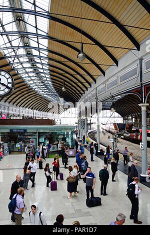 Passagiere warten am Bahnsteig in der Newcastle Hauptbahnhof mit Geschäften und Cafés an der Rückseite, Newcastle upon Tyne, Tyne und Wir Stockfoto