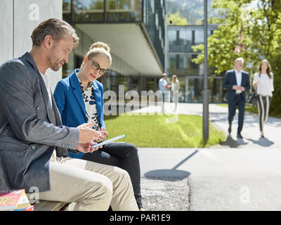 Kollegen mit Tablet sitzt auf der Bank außerhalb der Gebäude Stockfoto