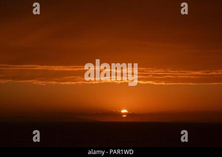 Schöne lodernden Sonnenuntergang Landschaft am über die Wiese und Orange Himmel darüber. Wunderbaren Sommer Sonnenaufgang als Hintergrund. Stockfoto