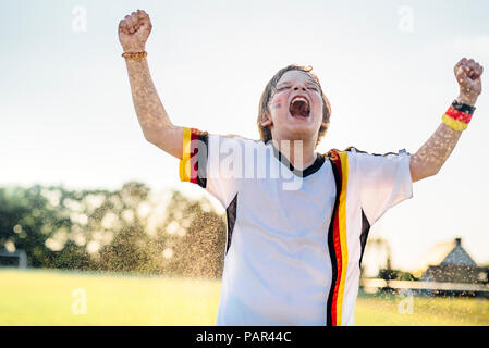 Junge tragen Deutsche Fussball shirt schreien vor Freude, stehend im Wasser spritzt Stockfoto