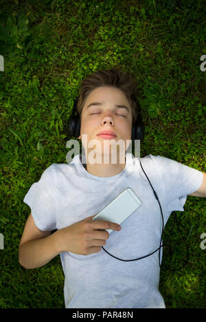 Portrait von Jungen liegen auf Wiese Musik hören mit Kopfhörern und Smartphone Stockfoto