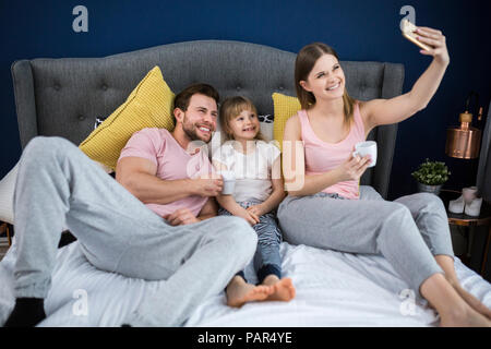 Glückliche Familie sitzt auf dem Bett, unter Smartphone selfies Stockfoto